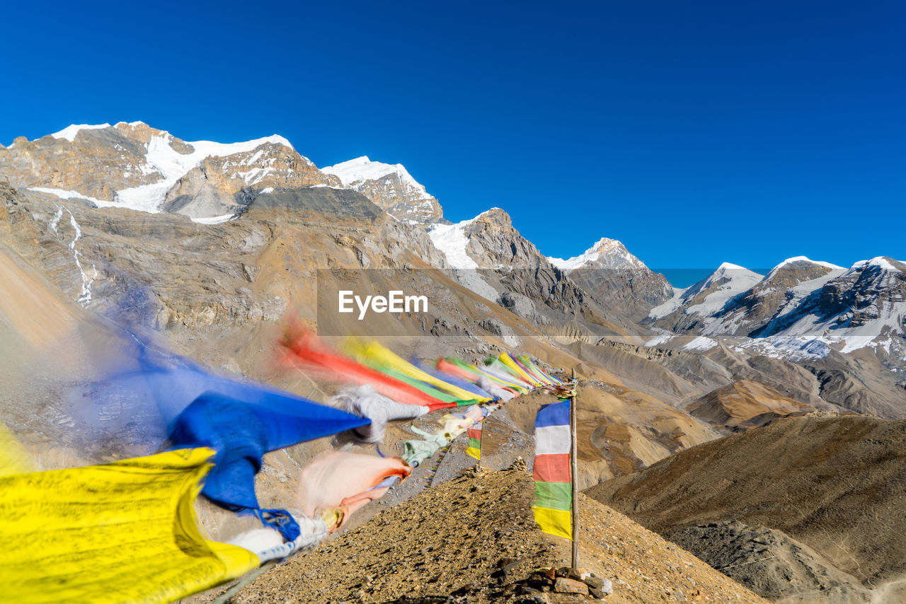 Flags flying by mountains against clear blue sky