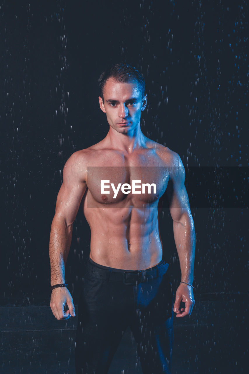 Portrait of shirtless man standing against black background