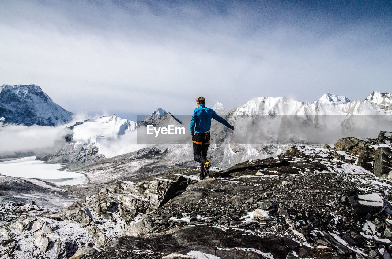 Full length rear view of man walking on landscape by snowcapped mountains against sky