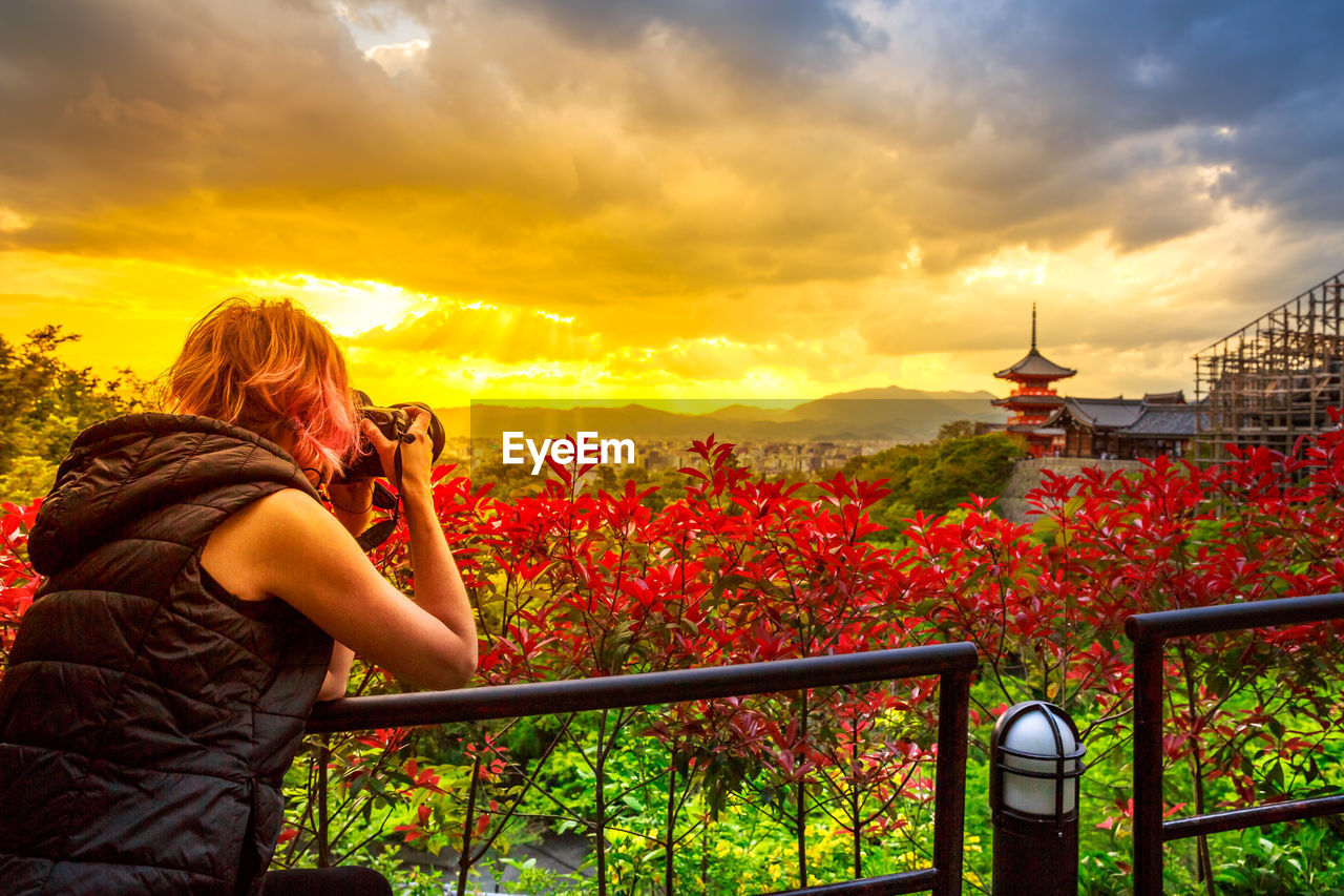 WOMAN PHOTOGRAPHING AGAINST ORANGE SKY