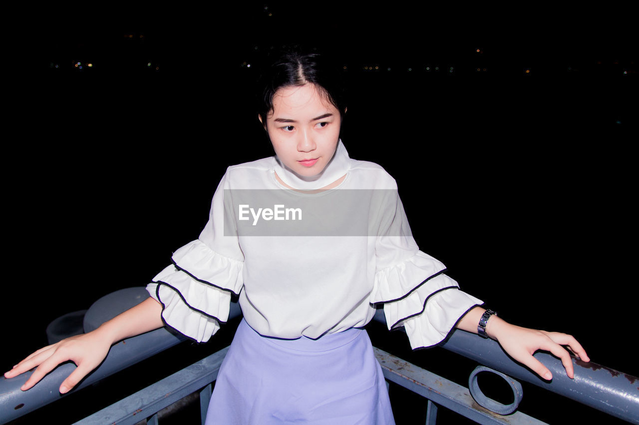 Thoughtful young woman standing against railing at night