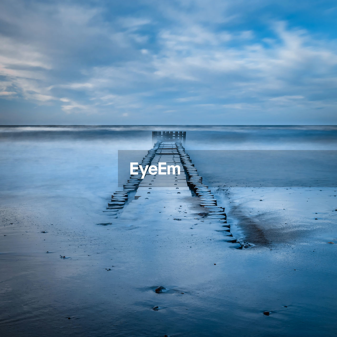 WOODEN POSTS ON BEACH AGAINST SKY