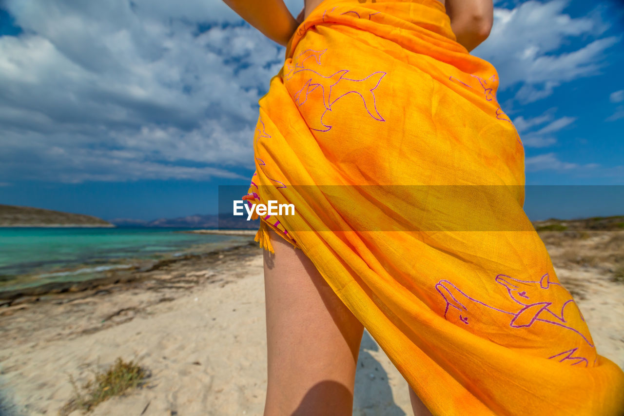 Low section of woman standing on beach against sky