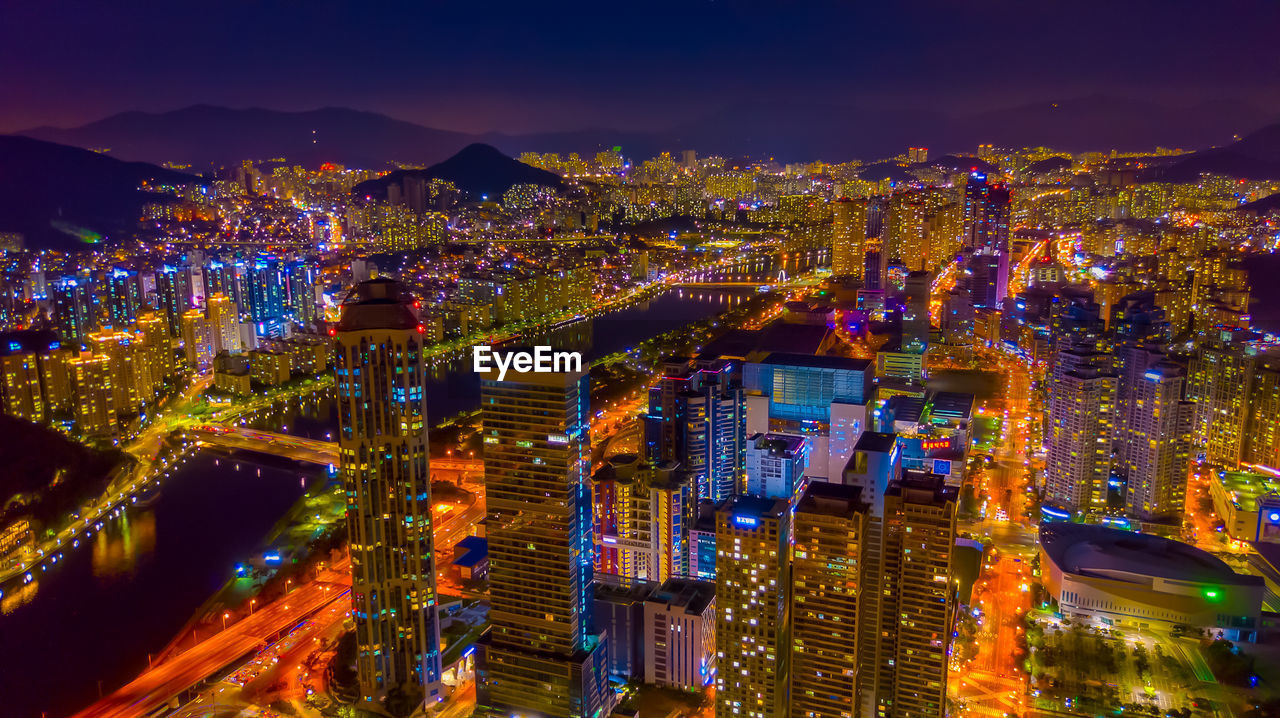 HIGH ANGLE VIEW OF ILLUMINATED CITY AGAINST SKY AT NIGHT