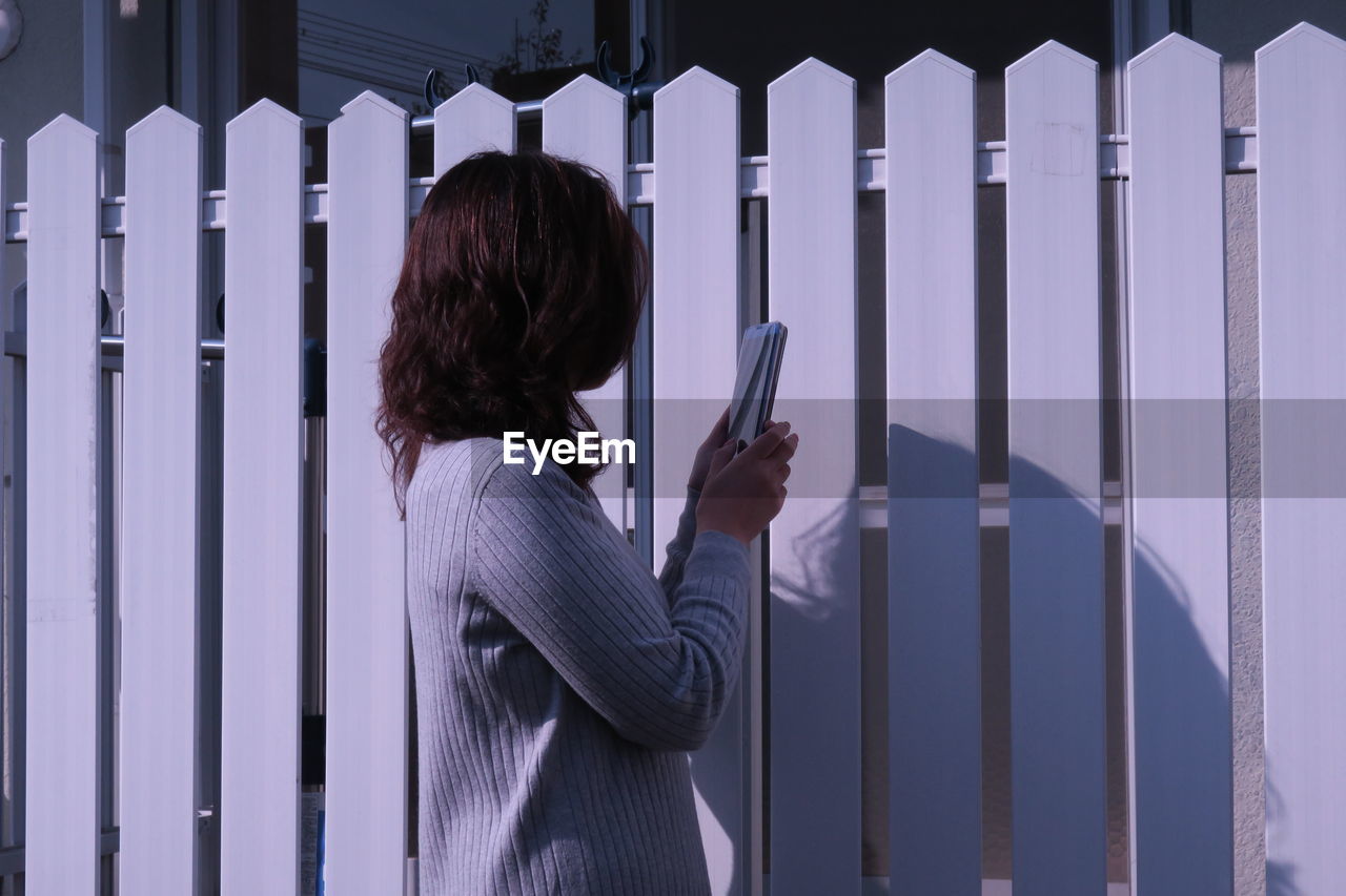 Side view of woman using phone by fence