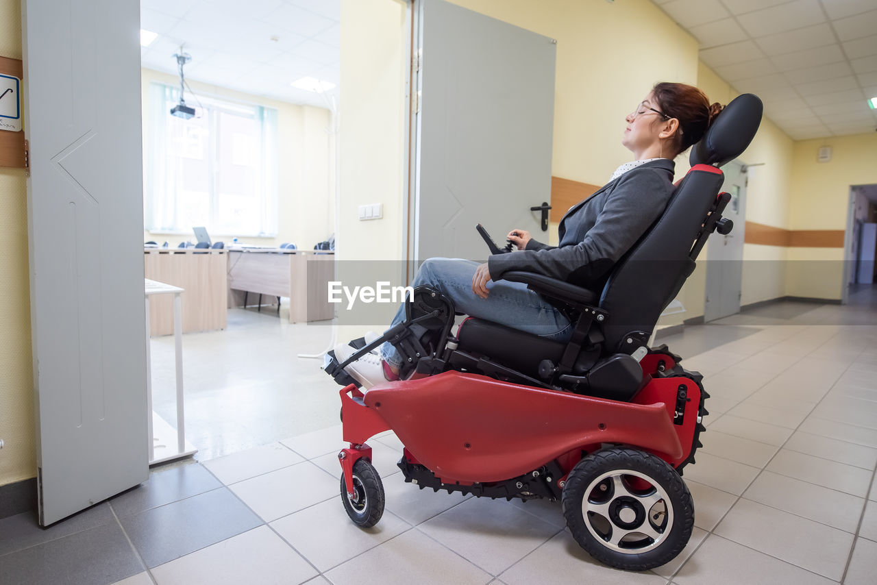 adult, full length, indoors, one person, baby carriage, side view, women, vehicle, young adult, transportation, sitting, business, travel, flooring, female, casual clothing, technology, healthcare and medicine, men