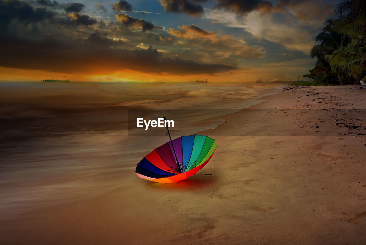 MULTI COLORED UMBRELLA ON BEACH DURING SUNSET