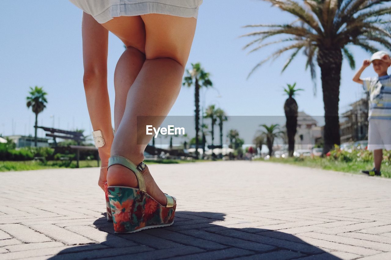 Low section of woman adjusting sandal while standing on street