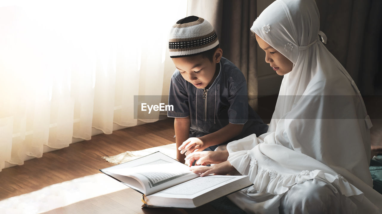 Cheerful sibling reading koran at home