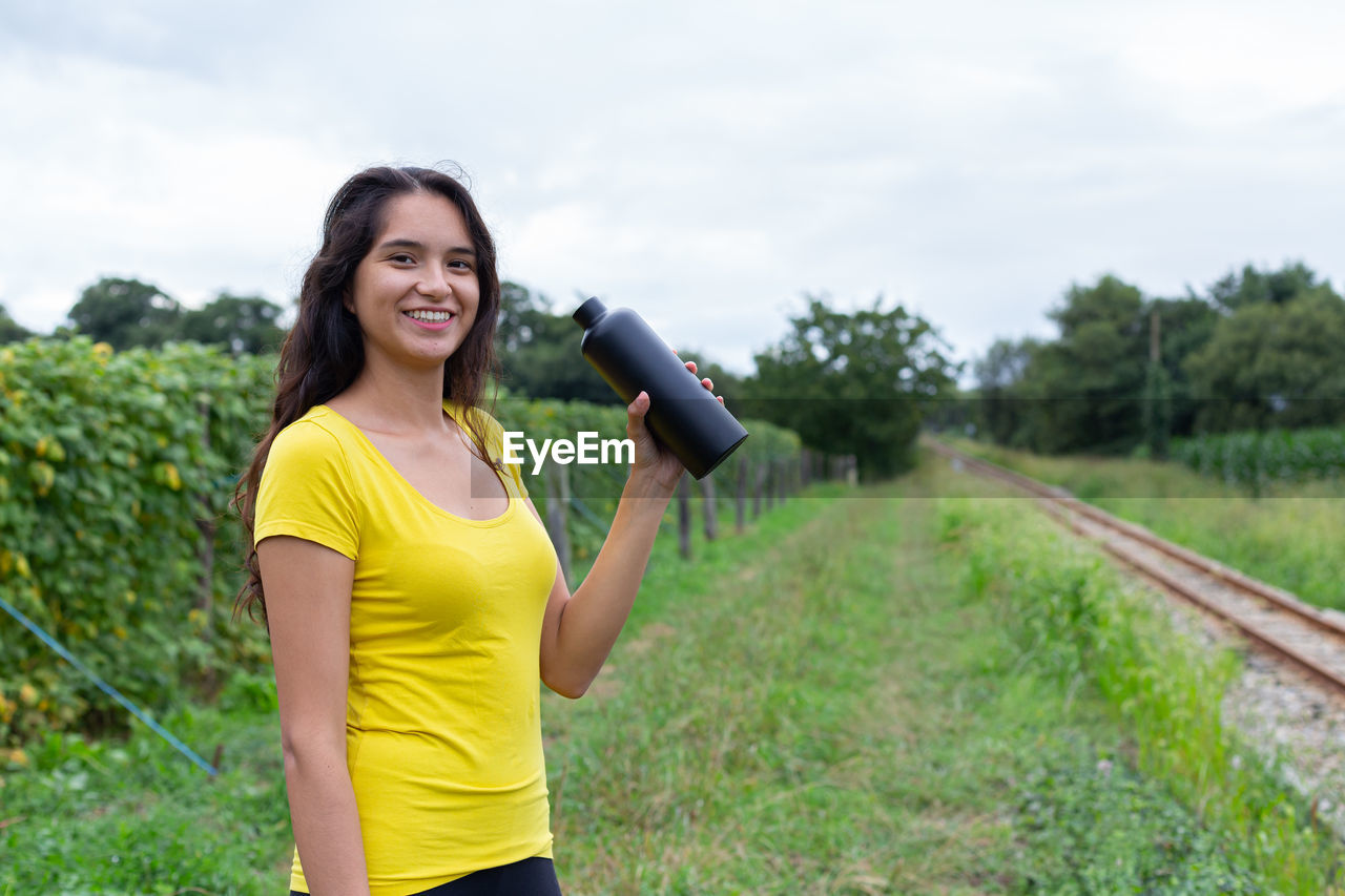 portrait of young woman standing on field against sky