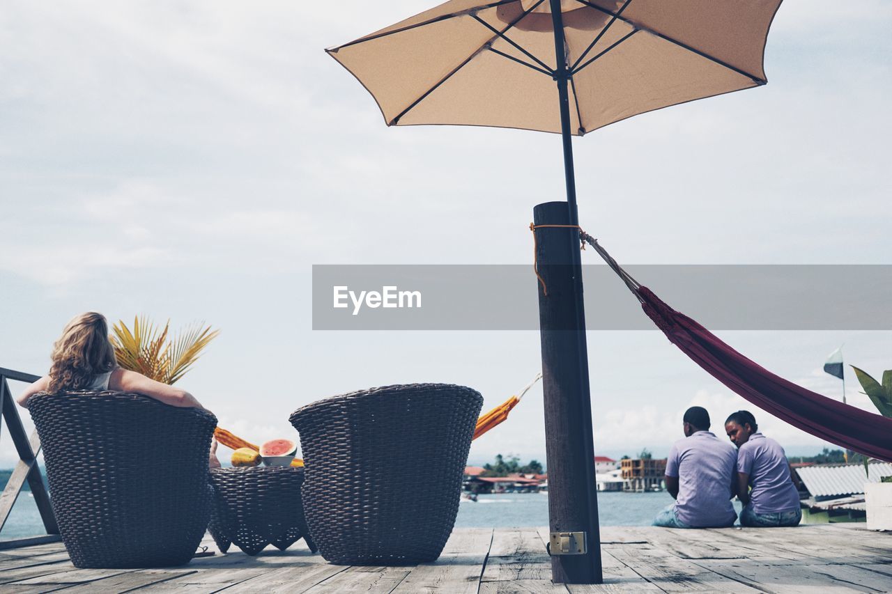 PEOPLE SITTING ON BEACH AGAINST SKY