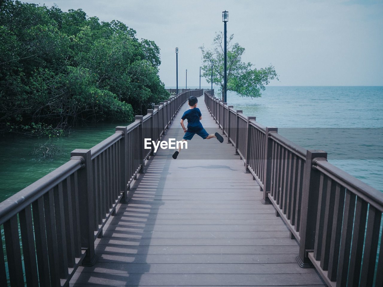 Boy jumping on walkway over sea against sky