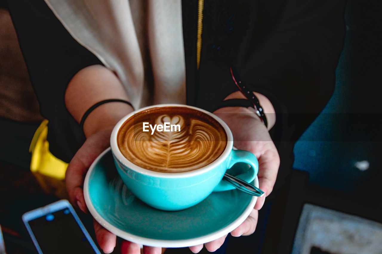 MIDSECTION OF COFFEE CUP WITH CAPPUCCINO SERVED IN BACKGROUND