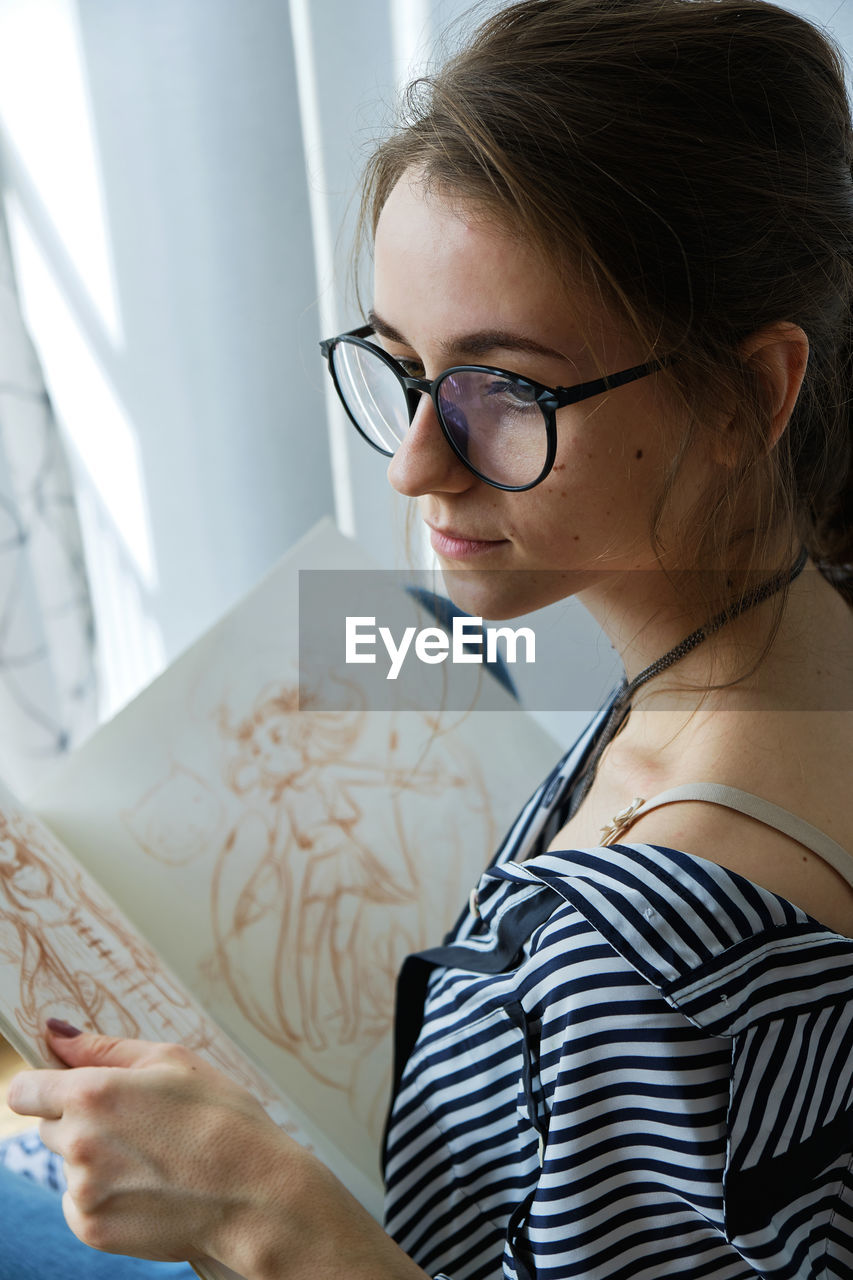 Millennial girl draws fabulous images on paper while sitting at home