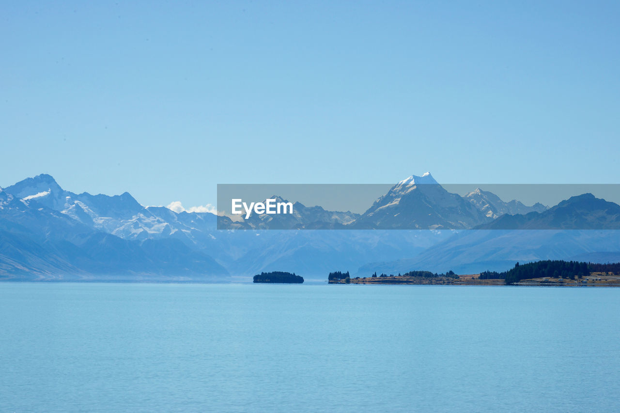 Scenic view of sea and snowcapped mountains against clear blue sky