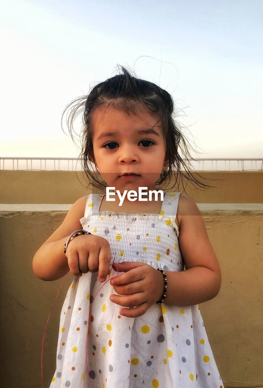 Portrait of girl standing by retailing wall against sky