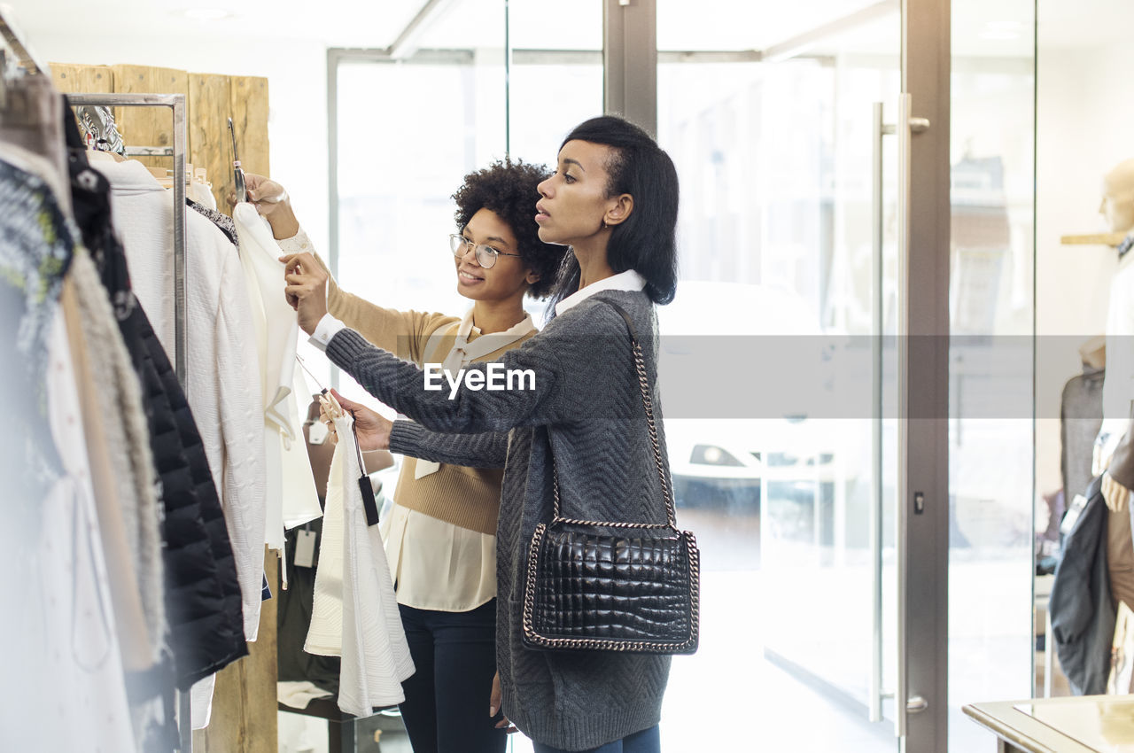 Friends choosing shirts on clothes rack by entrance at store on sunny day