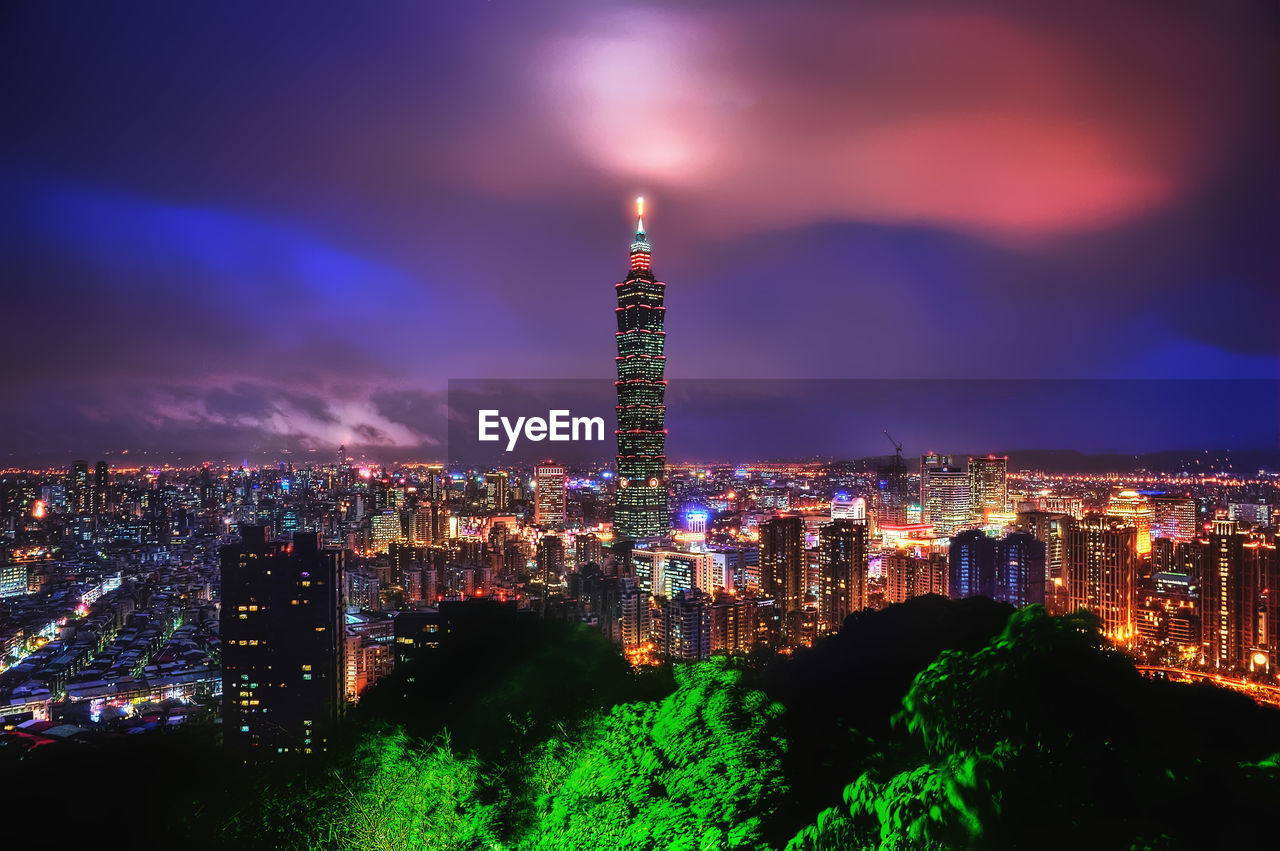 Illuminated buildings against cloudy sky at night