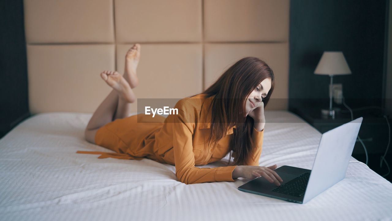 Young woman using laptop while lying on bed at home
