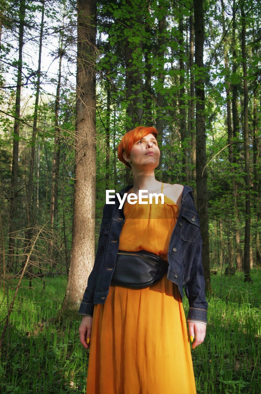 Young woman standing by tree in forest