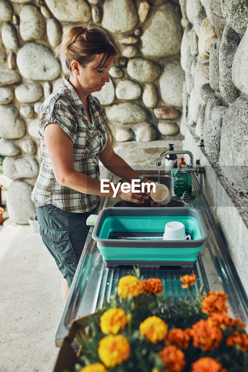 Woman washing up the dishes pots and plates in the outdoor kitchen during vacations on camping