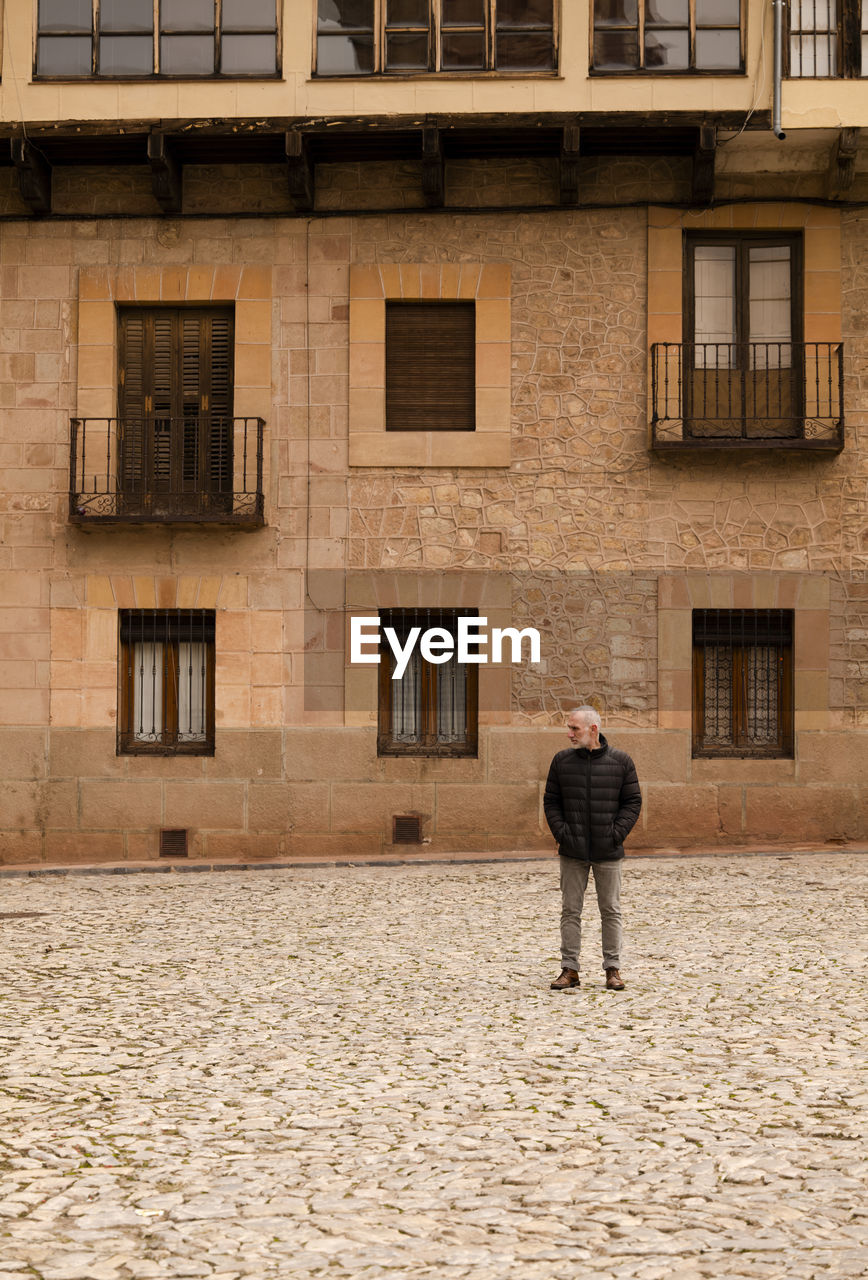 Adult man in winter clothes standing against old building. siguenza, castilla la mancha, spain