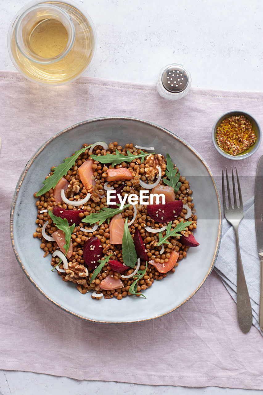 Closeup of a salmon and lentil salad seen from above on a table with a pink tablecloth