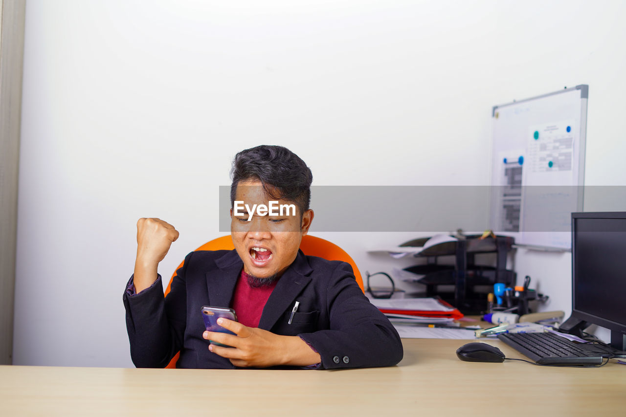 YOUNG MAN USING MOBILE PHONE ON TABLE