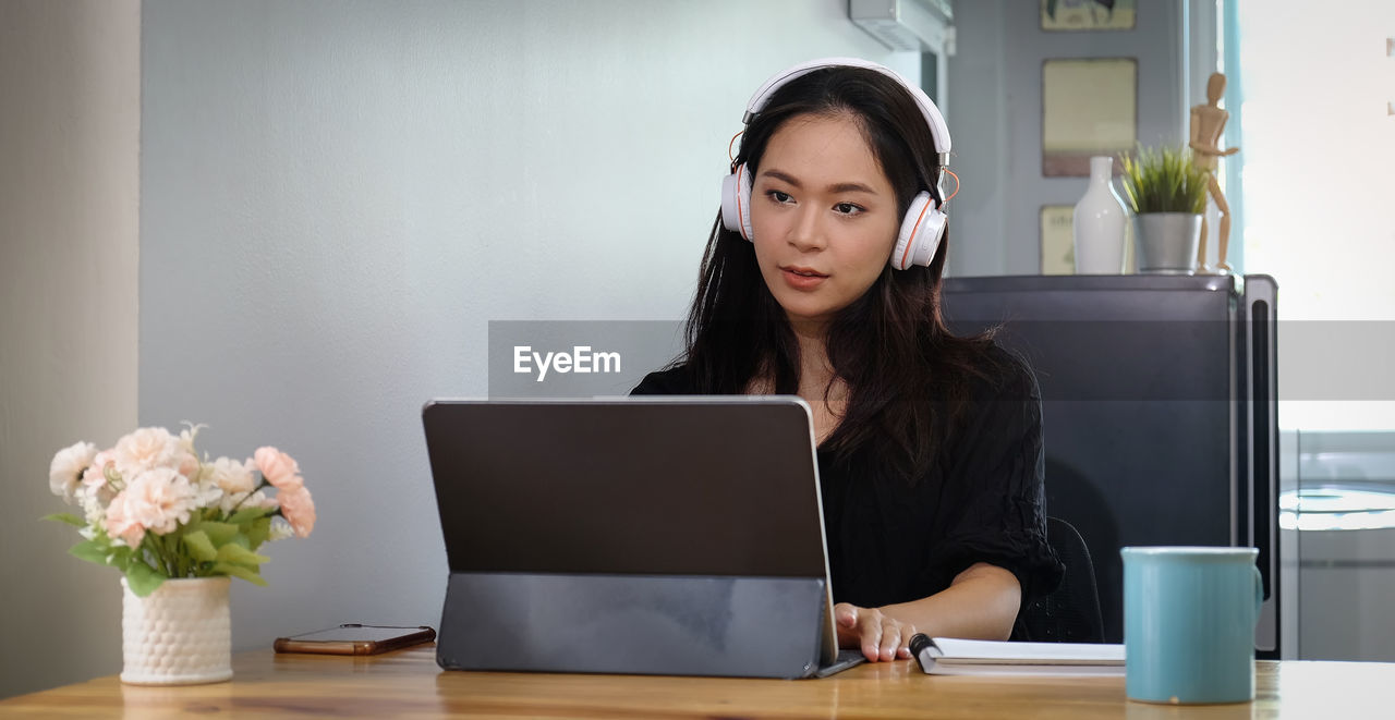 Businesswoman using laptop while wearing headphones