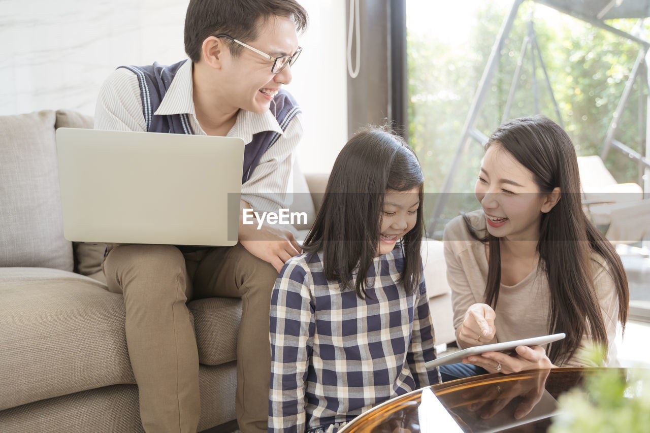 Smiling woman with daughter and man using digital tablet in living room at home