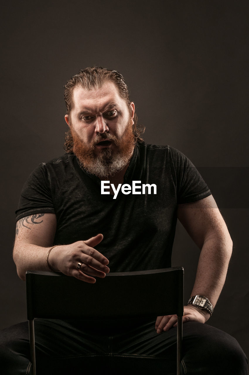 Surprised mid adult man gesturing while sitting against black background