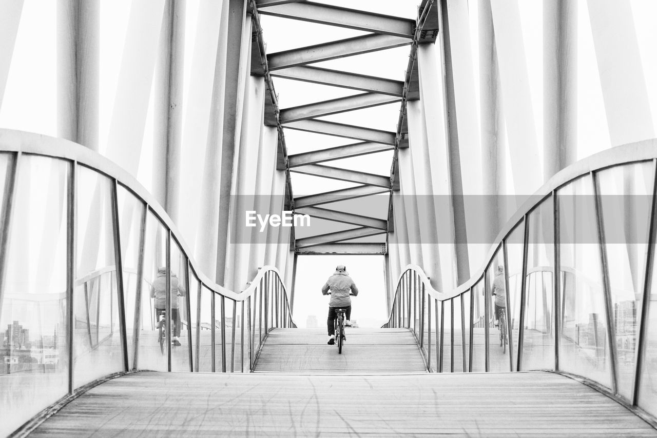 Rear view of person cycling on bridge