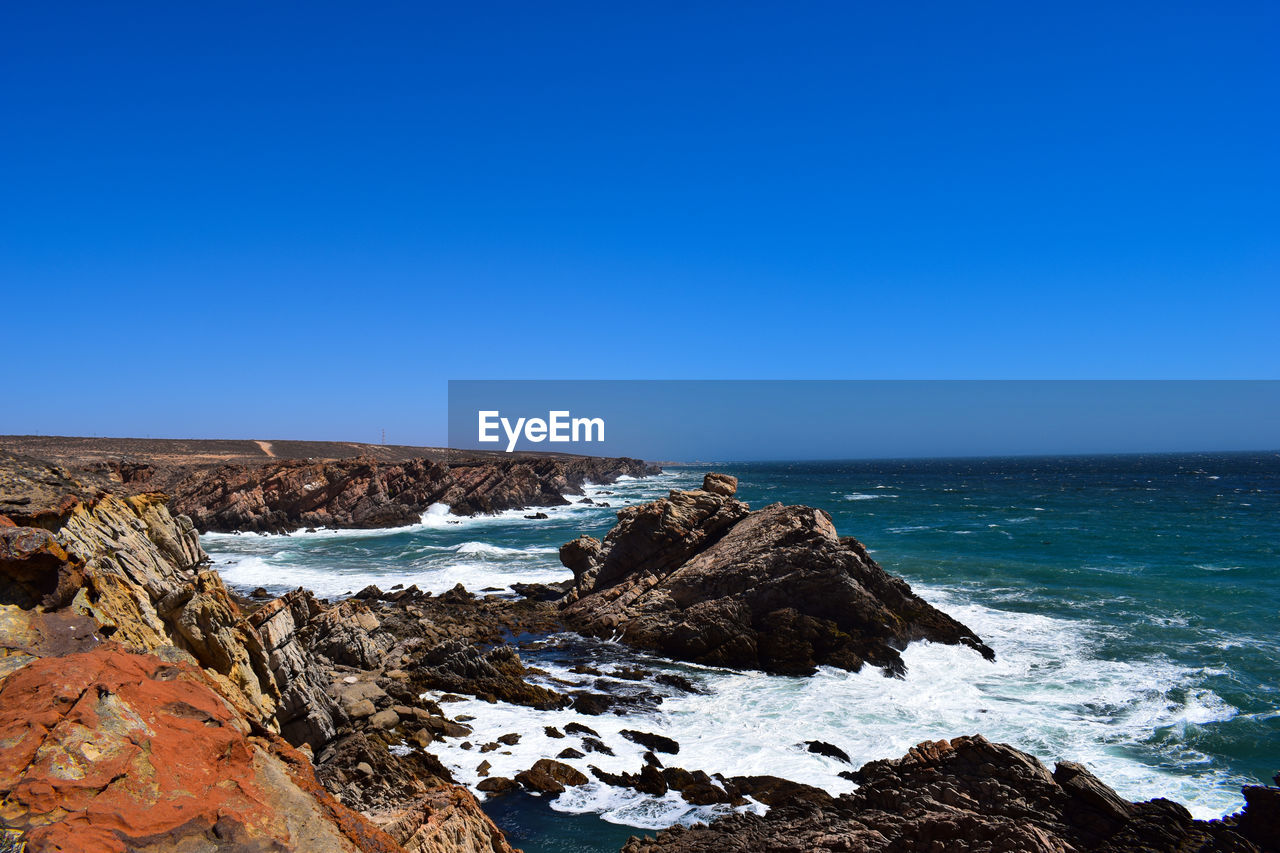 Rock formations in sea against clear blue sky