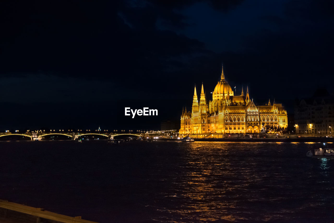 Illuminated parliament building by river against sky at night