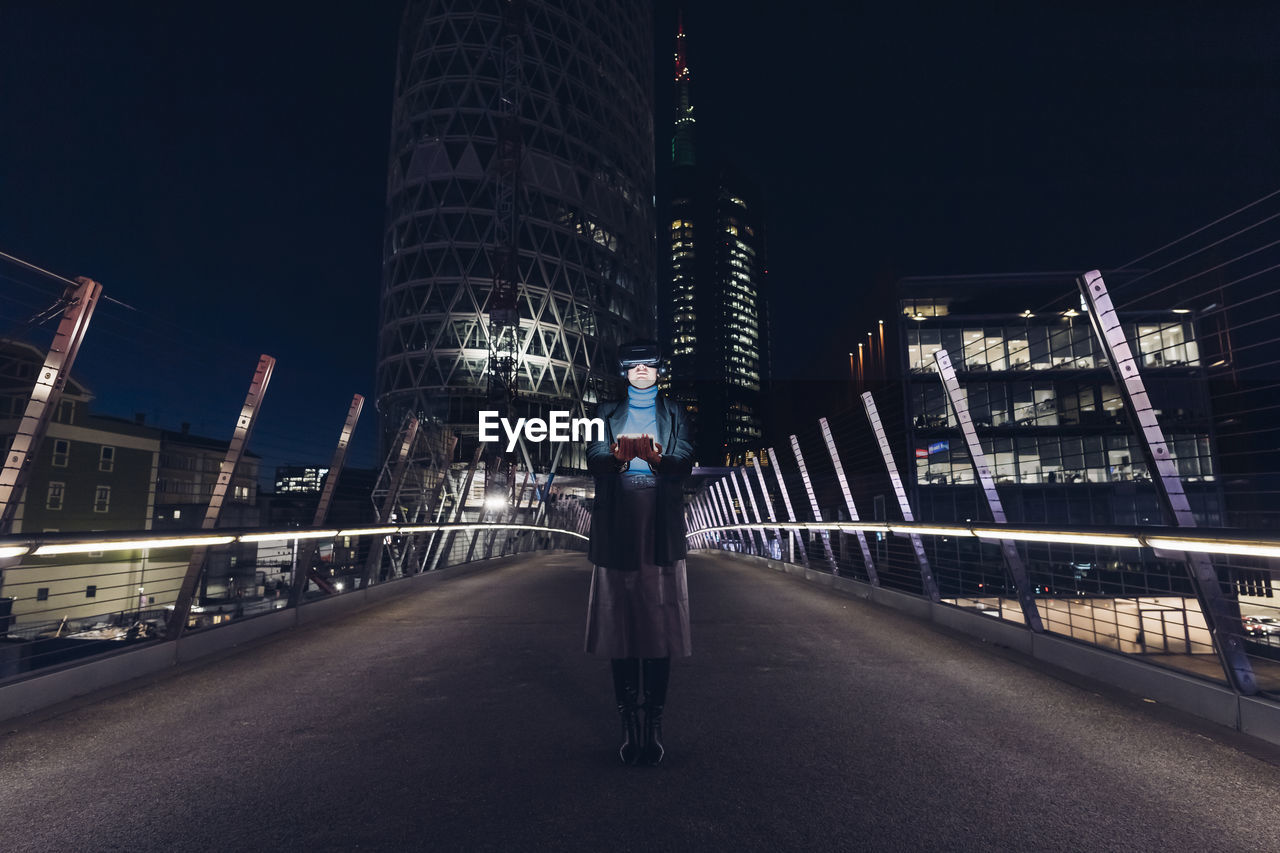 Businesswoman with virtual reality headset standing on bridge in city