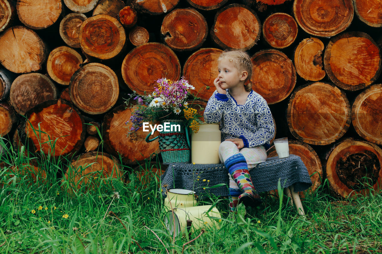 Rustic style, a girl in casual clothes sits on a bench against the background of a woodpile