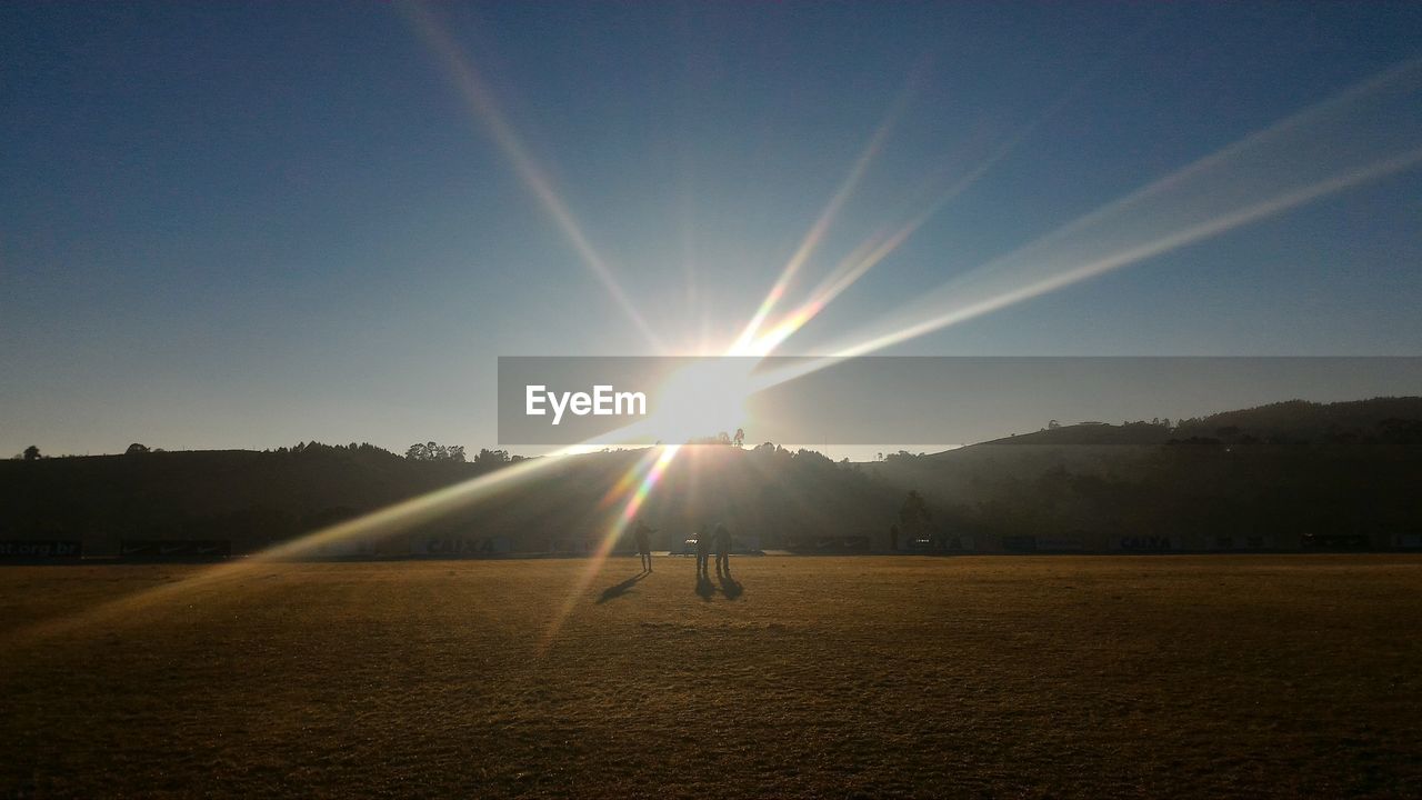 MAN STANDING ON FIELD AGAINST CLEAR SKY AT SUNSET