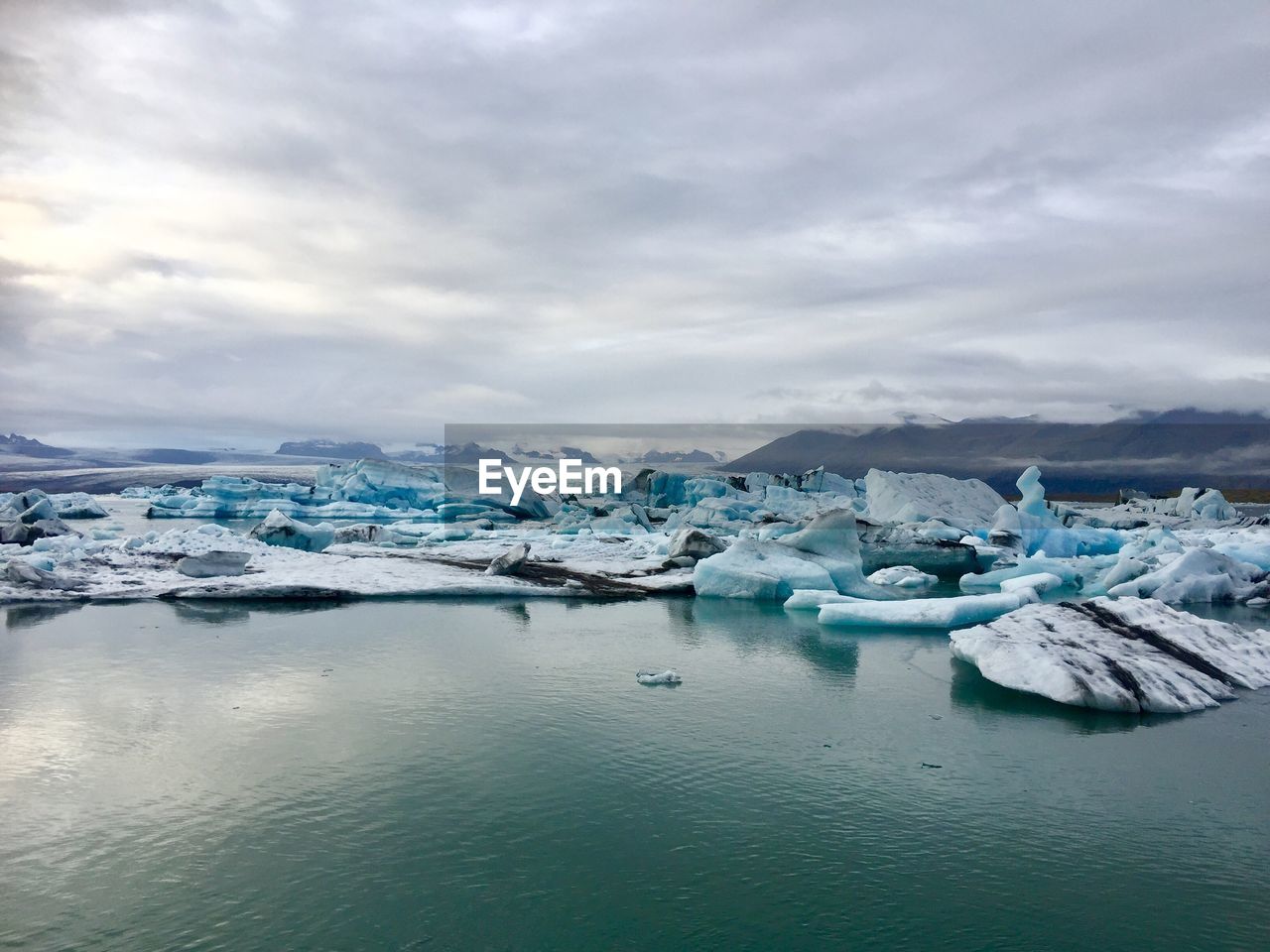 Ice bergs in sea against cloudy sky