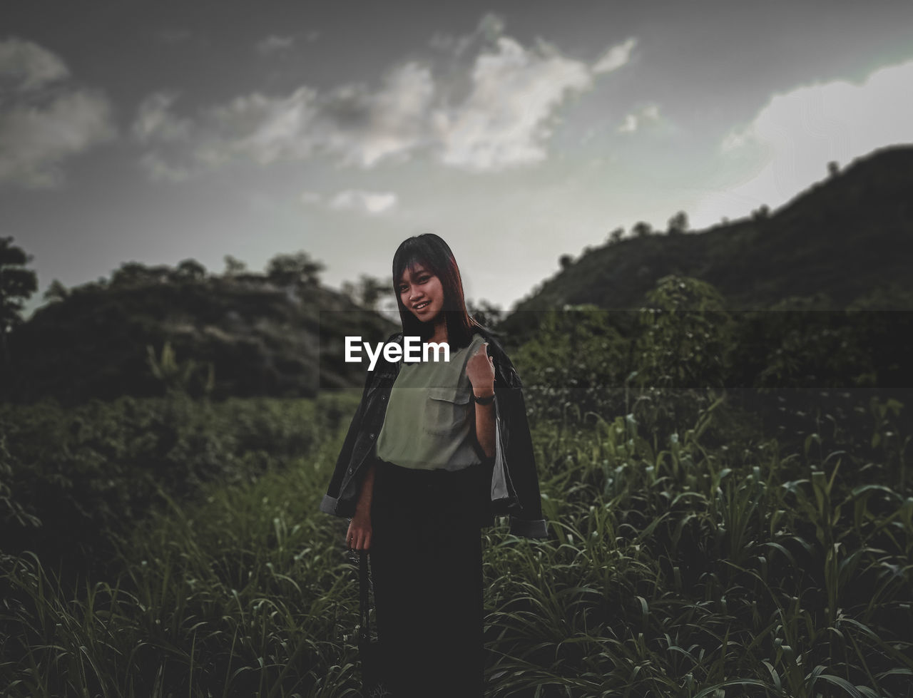 Young woman standing on field against sky