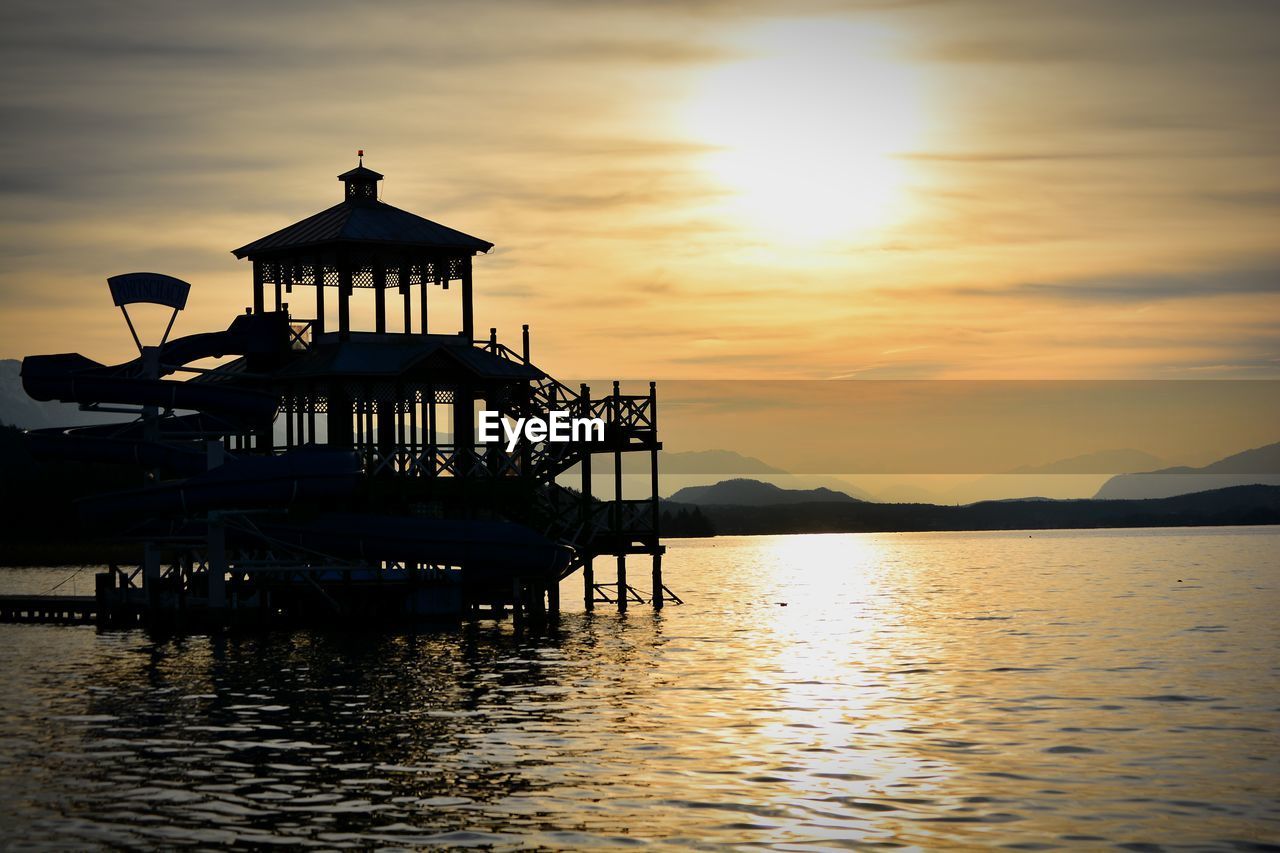 Silhouette built structure in sea against sky during sunset