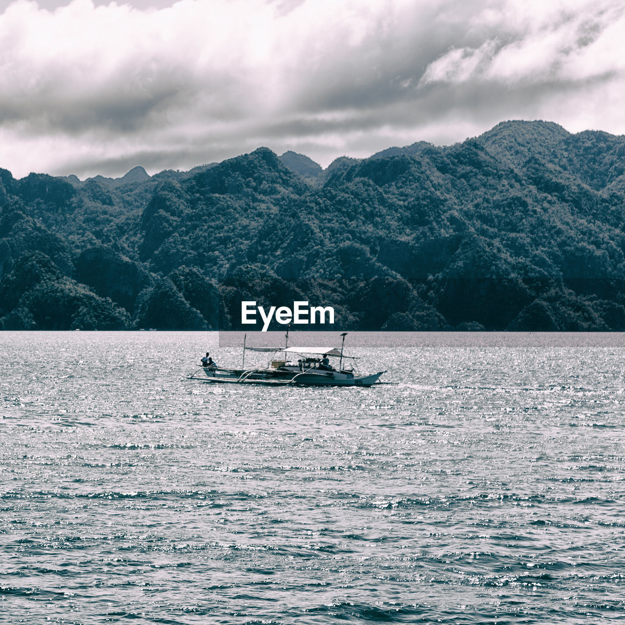 BOAT SAILING ON SEA AGAINST MOUNTAIN