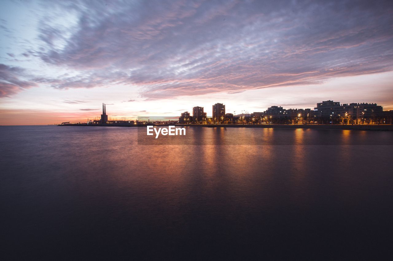 Scenic view of river by buildings against sky during sunset