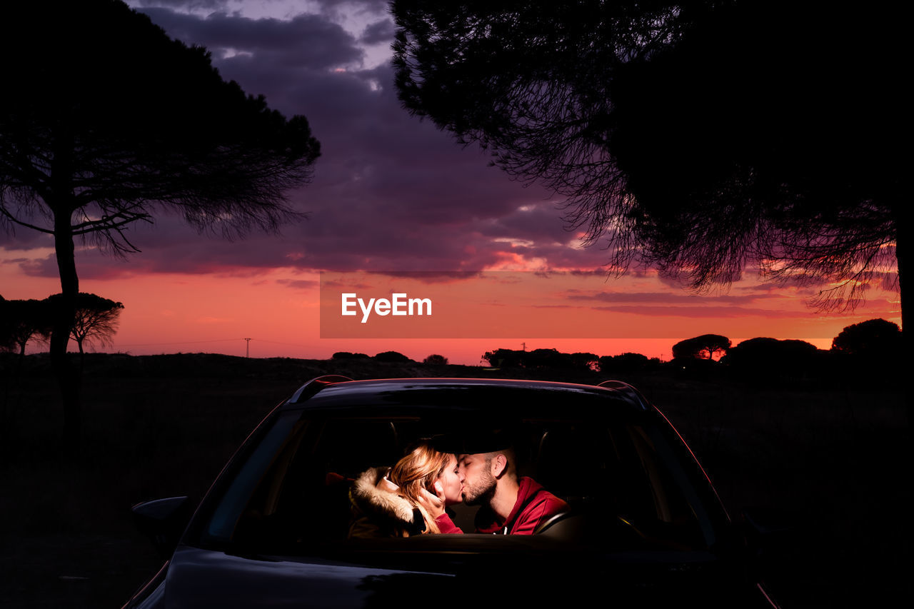 Young couple kissing in car during sunset