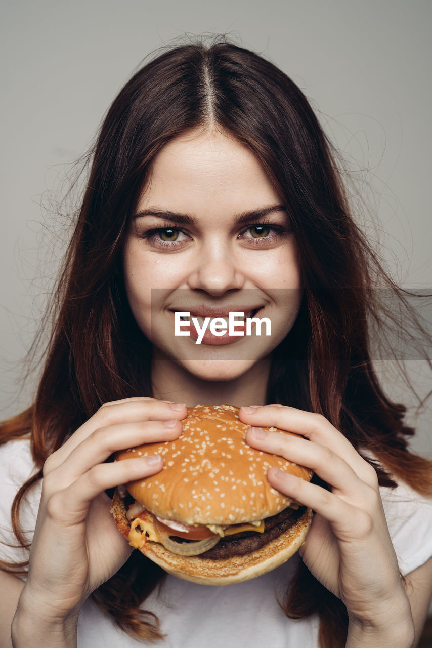 food, fast food, one person, food and drink, unhealthy eating, sandwich, hamburger, women, portrait, young adult, adult, eating, smiling, looking at camera, studio shot, long hair, happiness, bread, holding, indoors, meal, hairstyle, fast food restaurant, brown hair, emotion, meat, front view, cheese, take out food, cheerful, biting, person, hungry, teenager, snack, freshness, female, lifestyles, lunch, white background, child, enjoyment