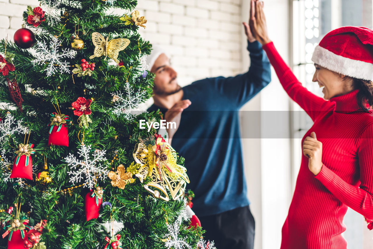 Cheerful couple high-fiving by christmas tree at home