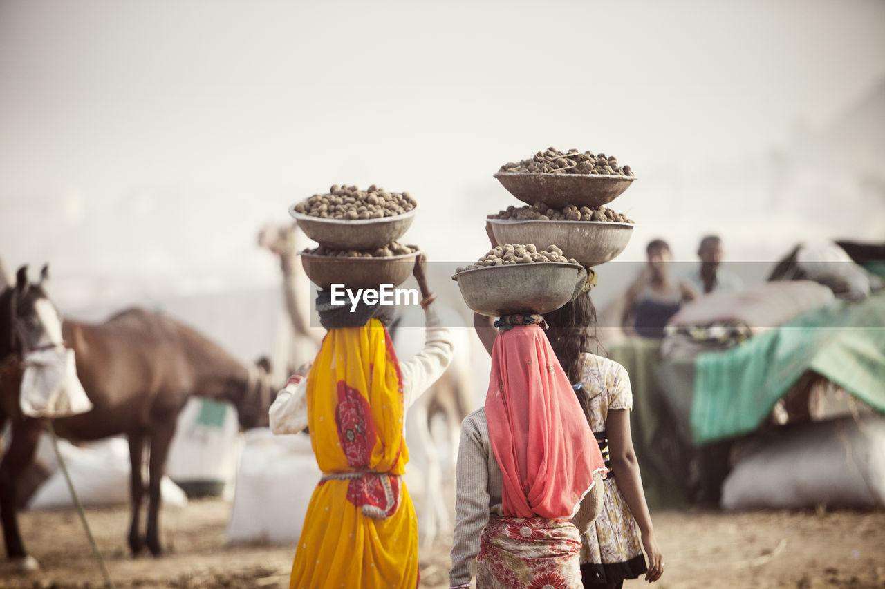 Rear view of women carrying dung in containers while walking at village
