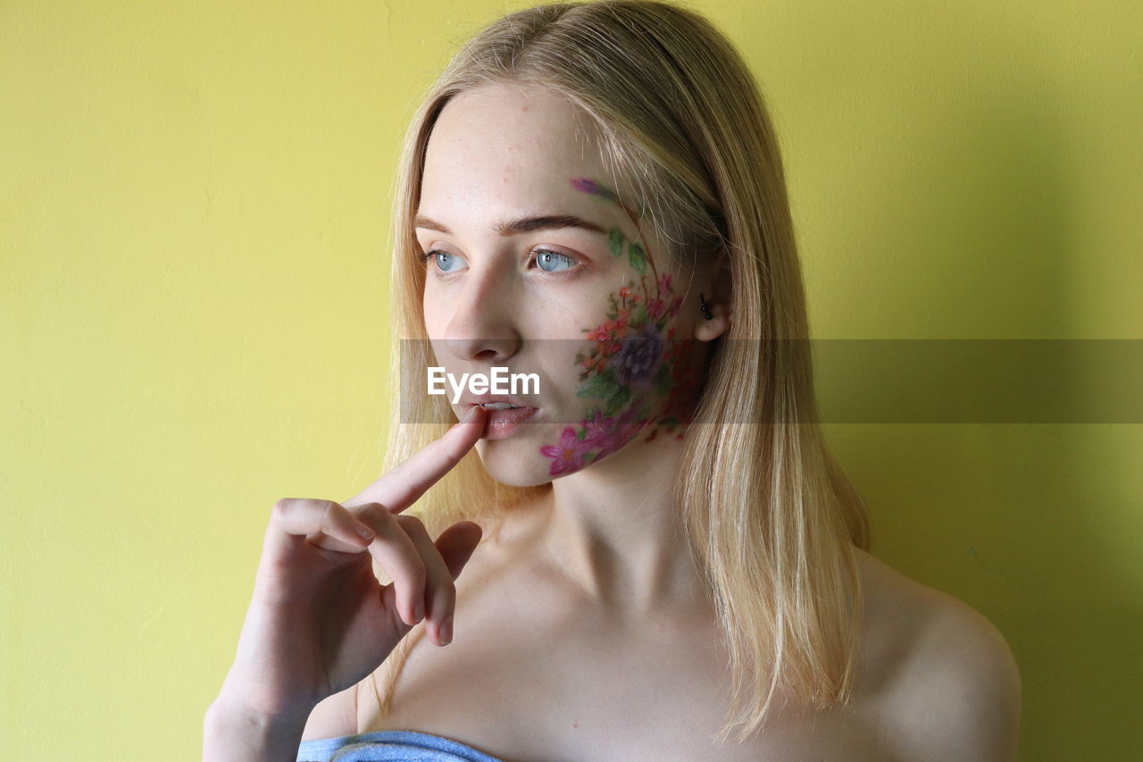 Young woman with painted face against yellow background