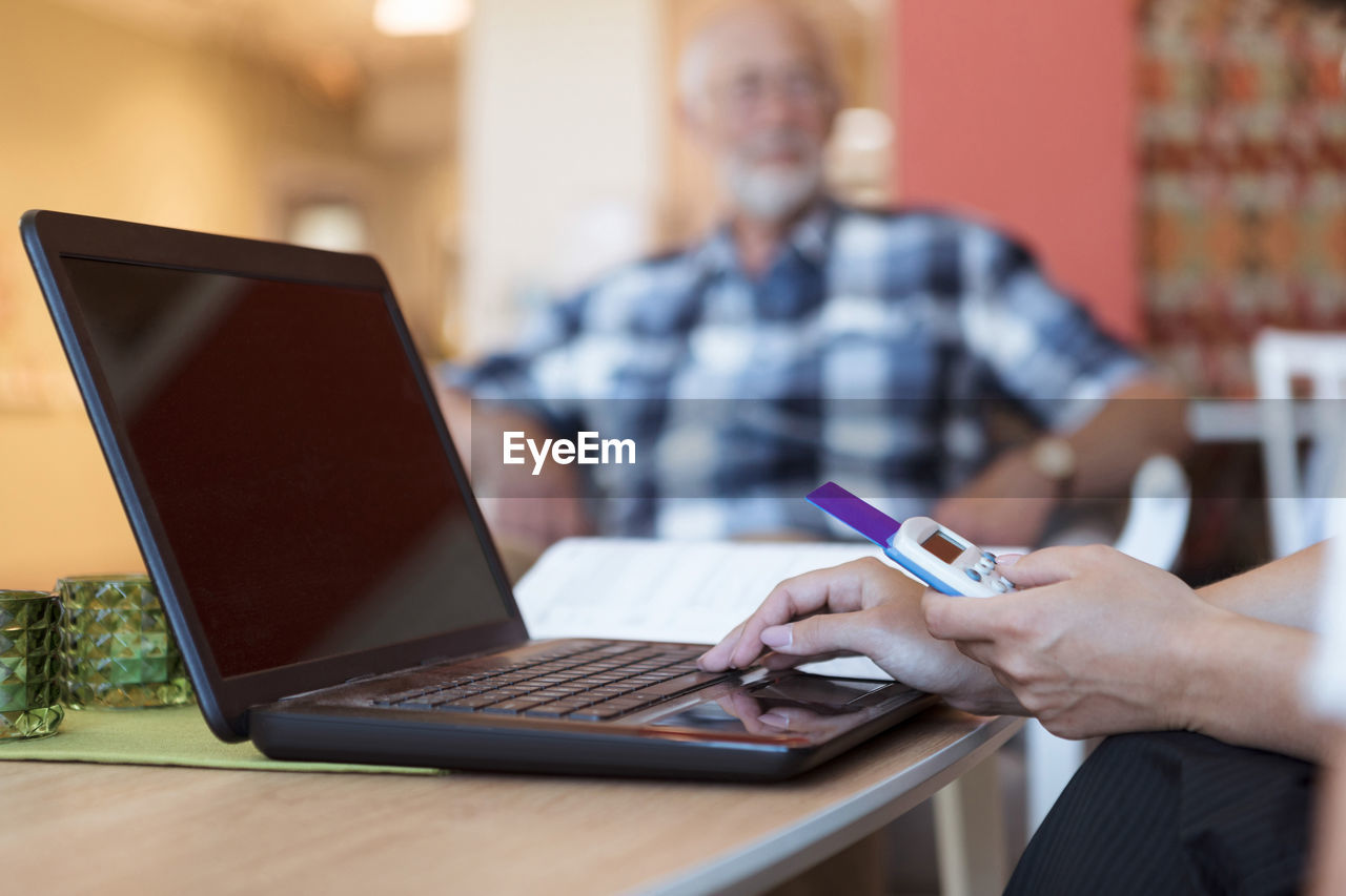 Cropped image of elderly care nurse buying medicine online using laptop and credit card at nursing home