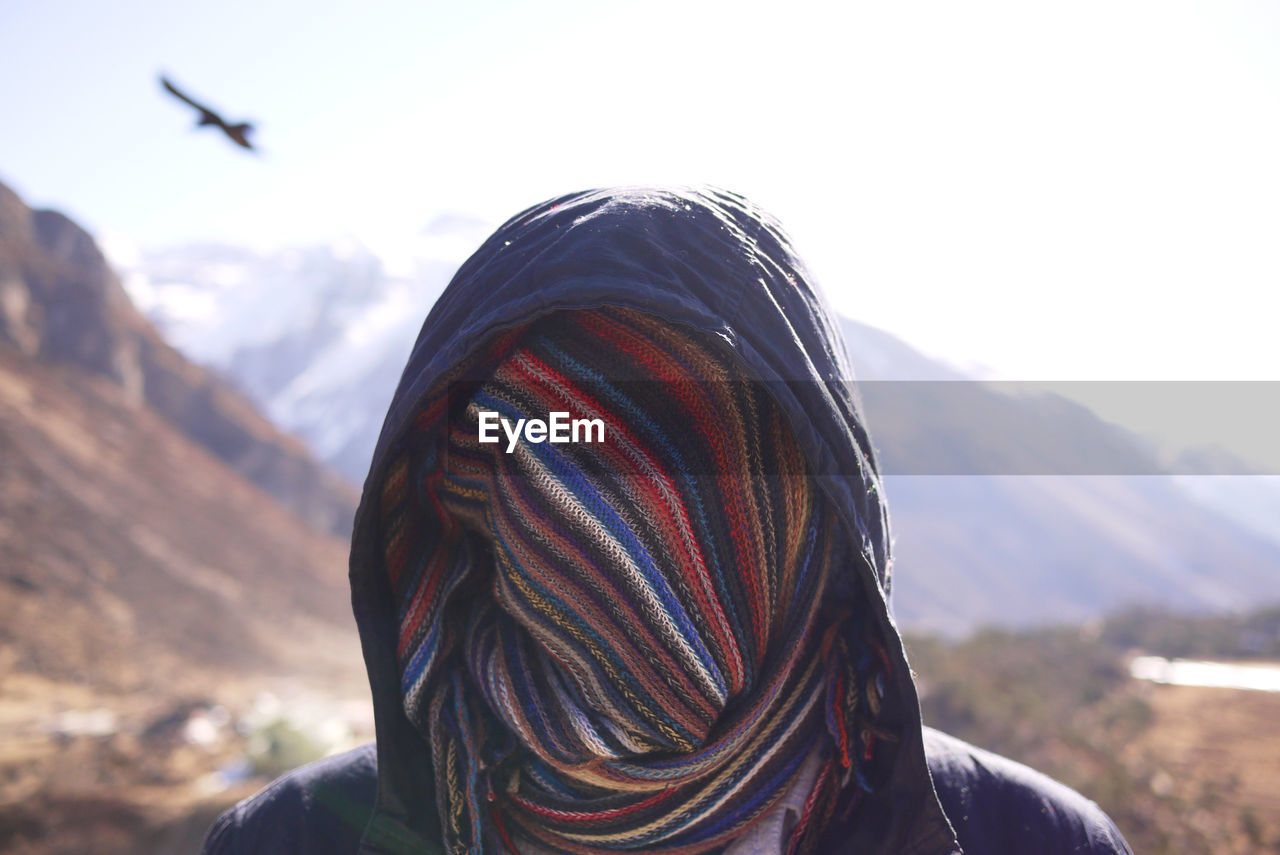 Person with face covered by scarf against mountains during winter