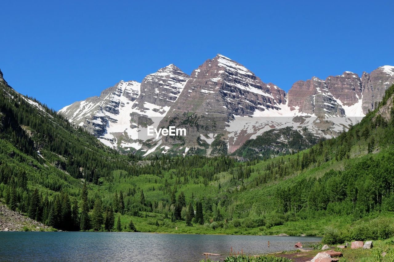 Scenic view of lake by maroon bells mountains against clear sky